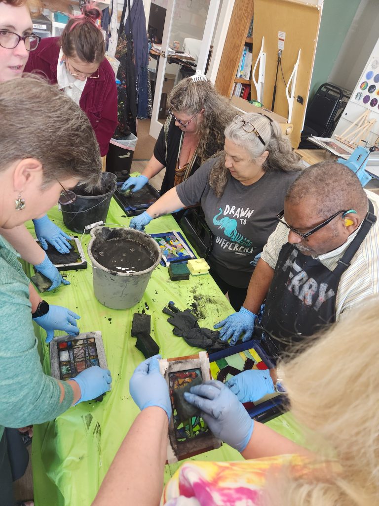 A group of artists add grouting to their mosaic glass artwork